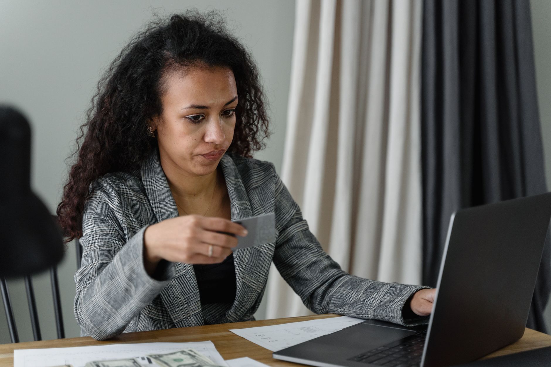 A person studies a laptop screen with a credit card and phone on a home desk, looking concerned.