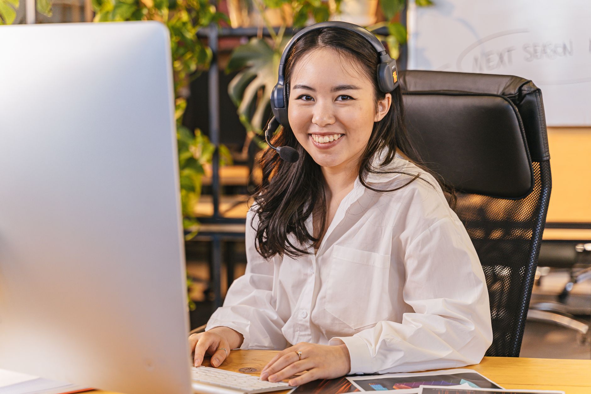 A person wearing a headset sits in a dim home office, speaking toward a computer screen that shows a support chat window.