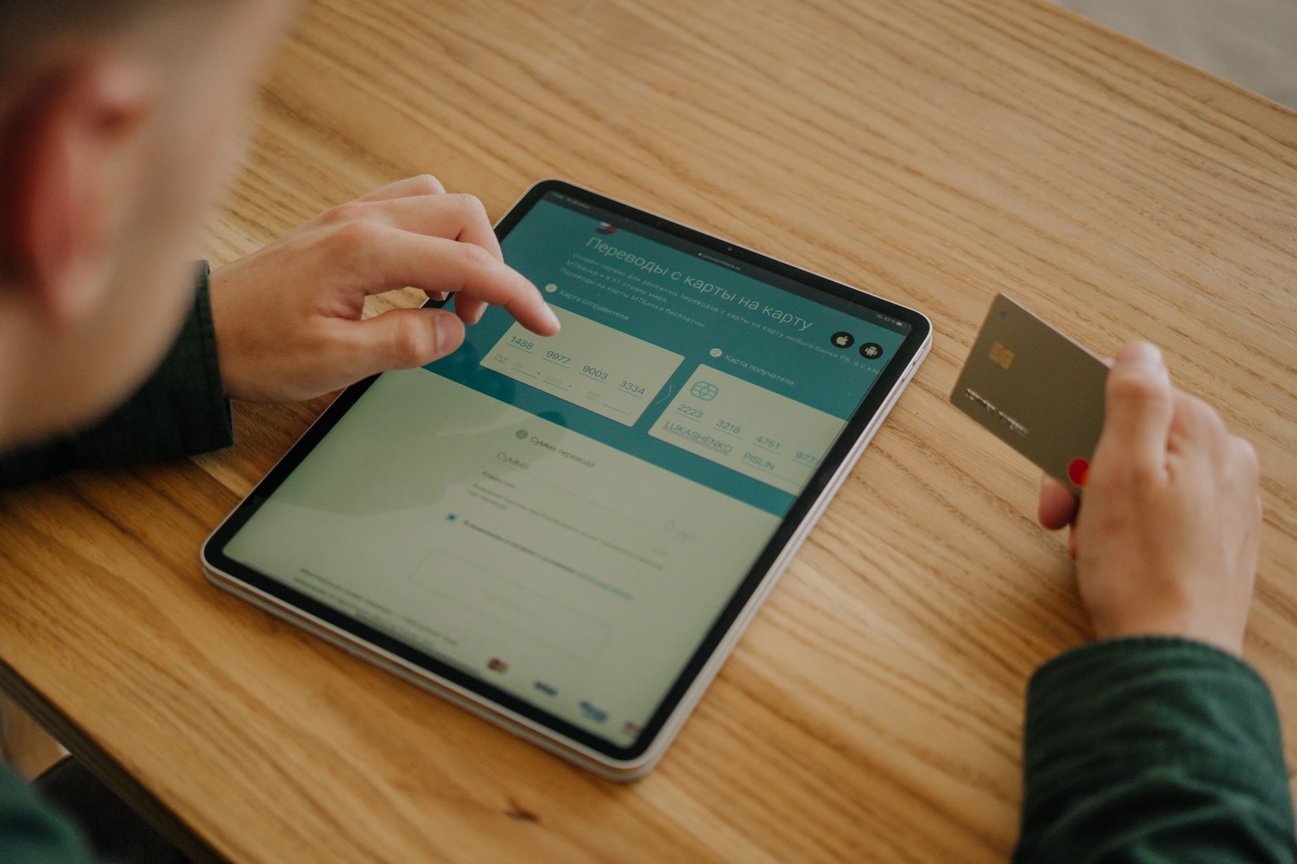 A person types on a laptop while holding a bank card and consulting a paper bill at a clean desk.