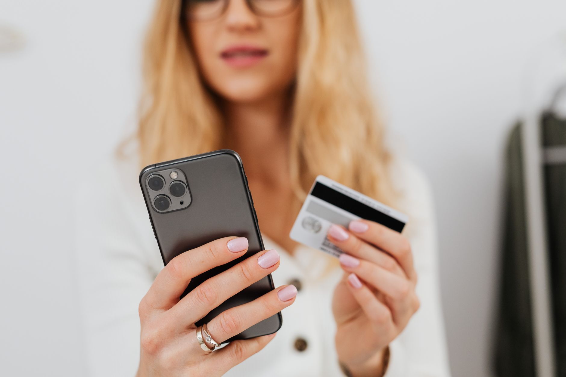 A woman holds a credit card and looks at her smartphone with a worried expression