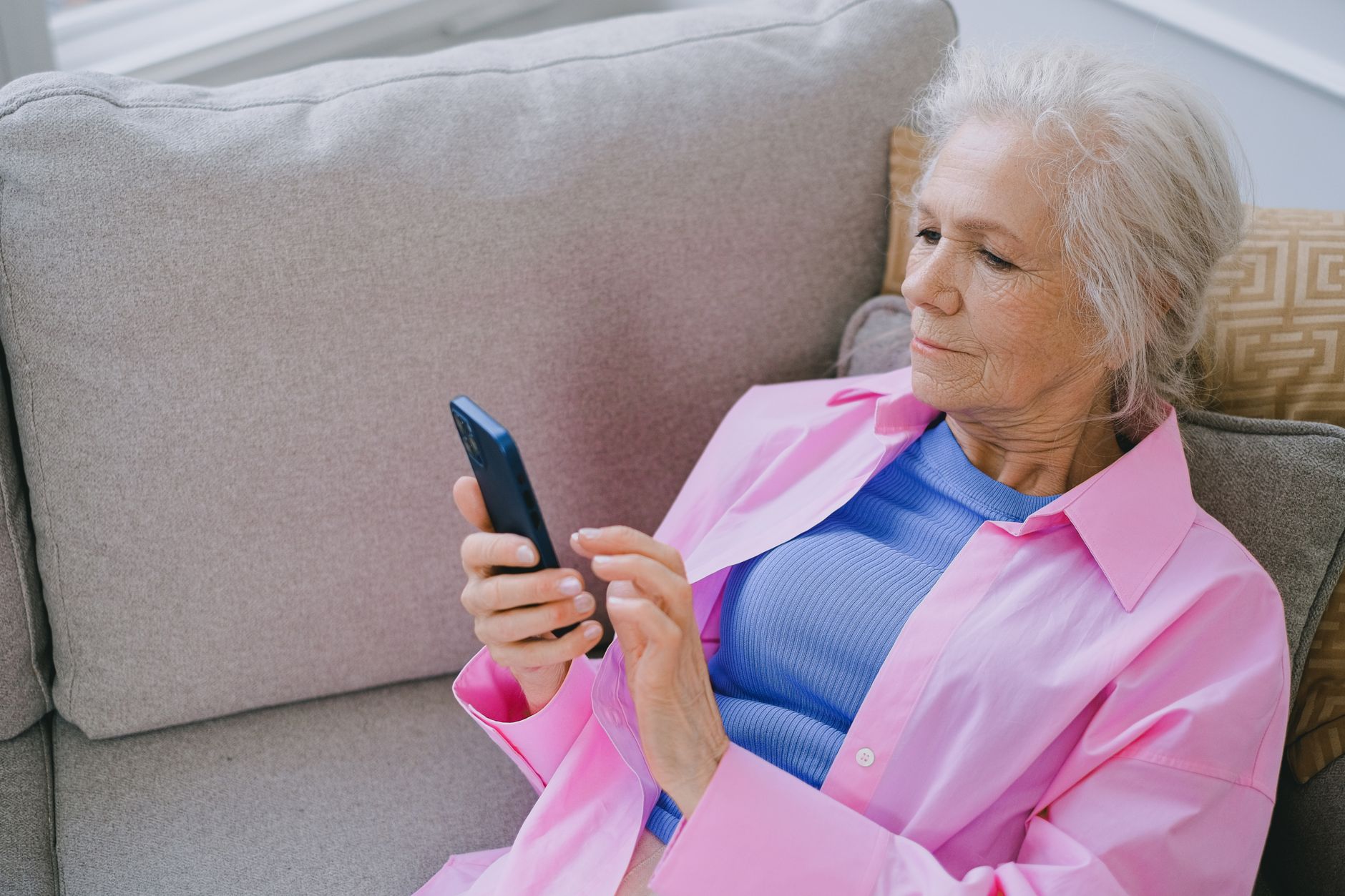an older adult looking at a smartphone with a confused expression while sitting at a kitchen table