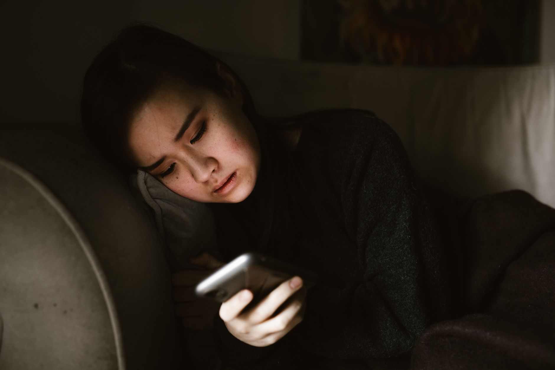 A concerned person holds a smartphone in a dim room, seeing an unfamiliar profile photo.