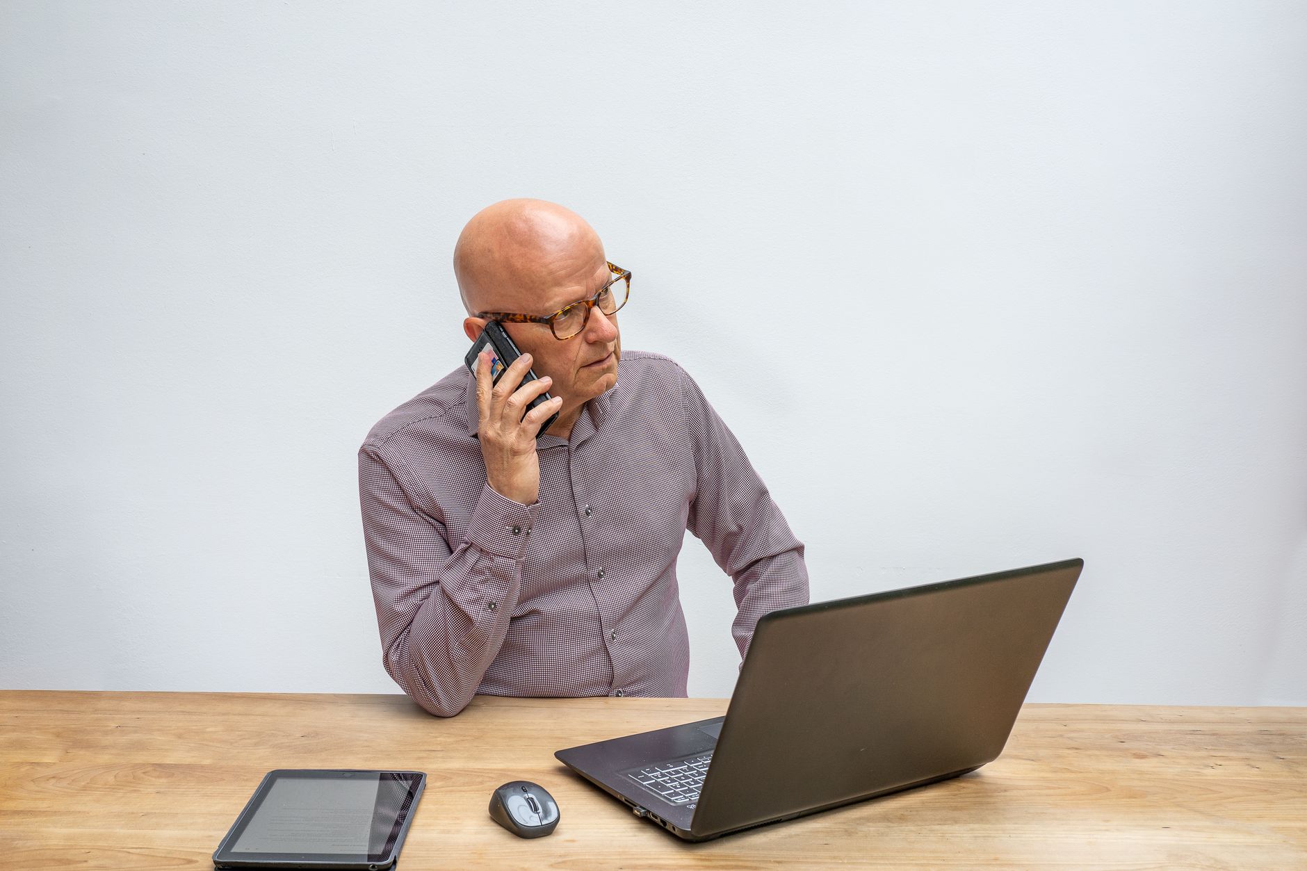 a person at a desk looking suspicious while holding a phone and looking at a laptop