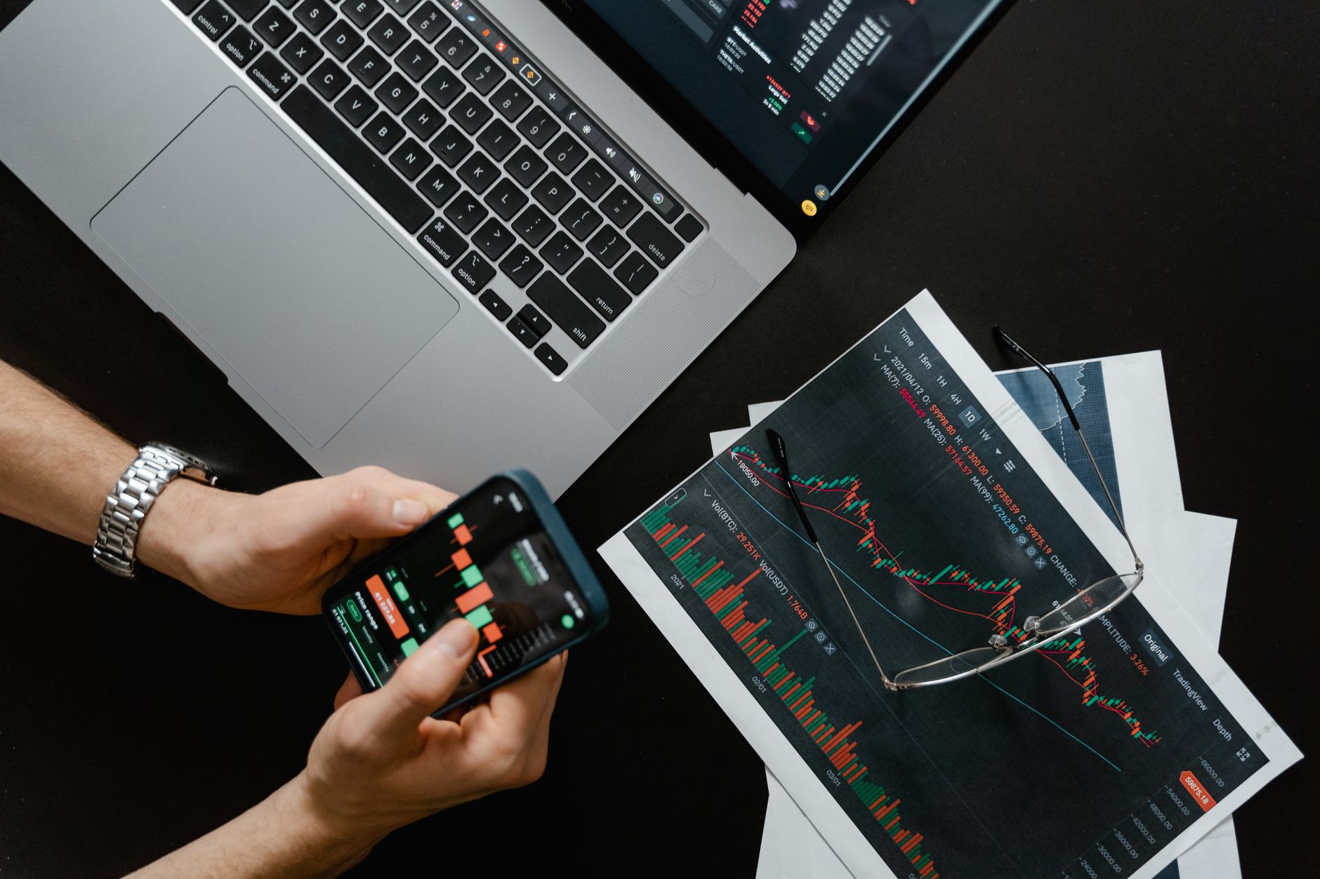 A laptop screen displays a colorful cryptocurrency trading chart while a smartphone sits beside it on a desk.