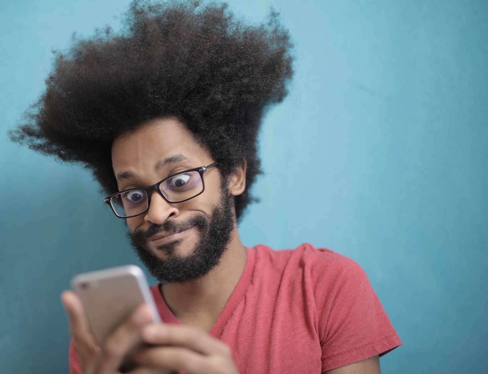 A person watches a smartphone with a shocked expression while sitting on a couch in a dim room