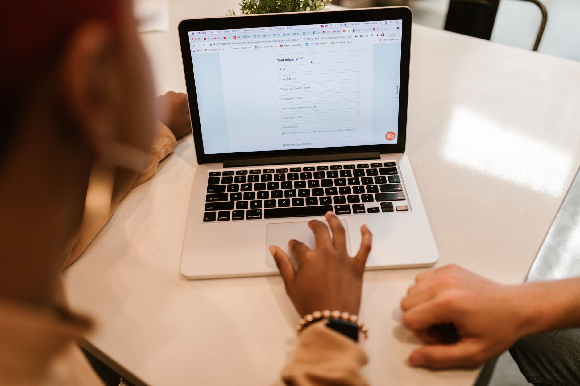 A person at a home desk typing on a laptop with an online form on screen