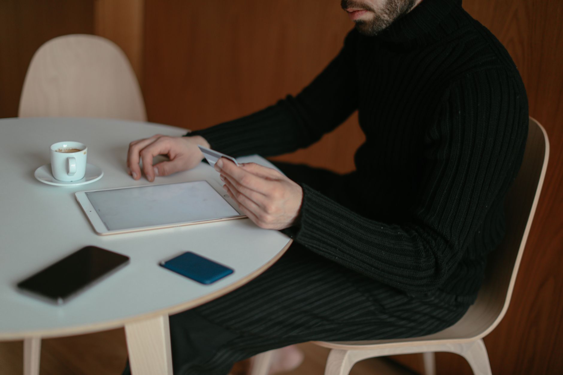 A person on the phone holding a credit card at a kitchen table with a laptop open